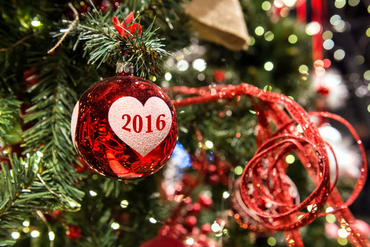Red christmas ball with number 2016 on the white heart is on the Christmas tree