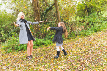 Mother and daughter playing with leaves at park in autumn