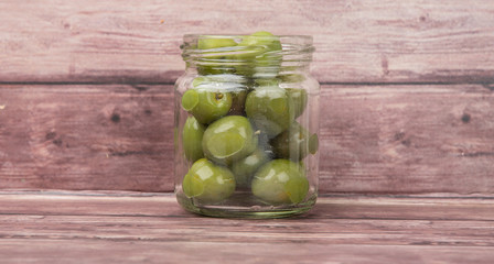 Pickled green olives in mason jar over wooden background