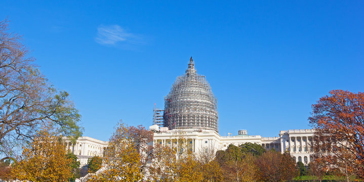 The west front of the United States Capitol with dome restoration scaffolding in autumn. The US Capitol building on a sunny afternoon in Washington DC.