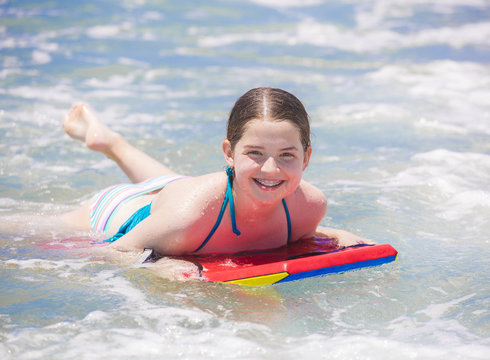 Cute young teenager smiling with braces while on a boogie board and playing in the ocean waves