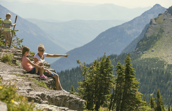 A family sitting together on a rocky ledge looking at a gorgeous view while visiting Glacier National Park in the Rocky Mountains