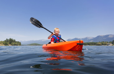 Young Boy paddling a kayak on a beautiful mountain lake. Low angle view of the nature's beauty © Brocreative