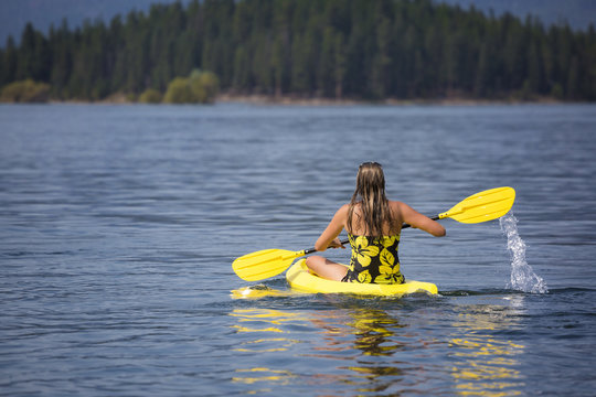 Beautiful fit and active woman paddling her kayak on a scenic, peaceful mountain lake
