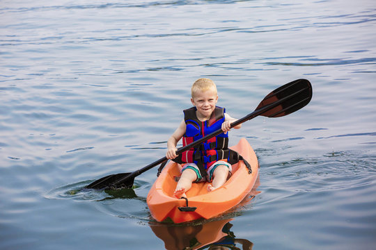 Young Boy Paddling A Kayak On A Beautiful Lake