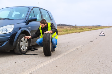 Mechaninc trying to repair a flat tire on the car by the road