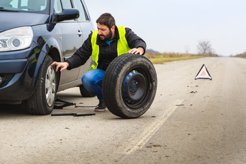 Fototapeta na wymiar Man chaning a flat tire on his car