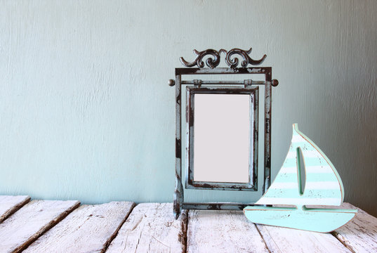 image of old victorian steel blue blank frame and wooden sailing boat on wooden table

