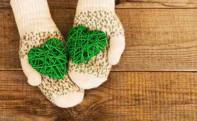 Woman hands in light teal knitted mittens are holding green hear