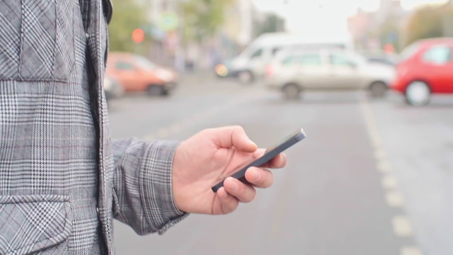 Close-up of man walking across the street and using his smartphone