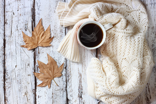 top view image of white cozy knitted sweater with to cup of coffee and autumn leaves on a wooden table
