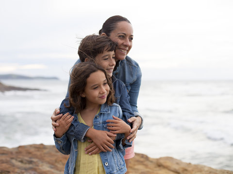 Madre abrazando a sus hijos junto al  mar