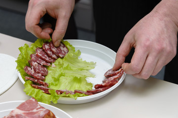 Man sliced sausage on white plate with leaf of salad	