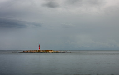 Fototapeta premium Red lighthouse on small island, on background cloudy sky.