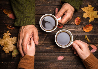 Old people holding hands on rustic table covered with autumn leaves