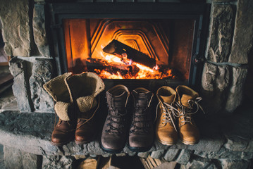 Winter boots in front of a fireplace. Family vintage folk boots drying near the fireside. Warm cozy...
