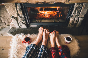 Bare couple feet by the cozy fireplace. Man and Woman relaxes by warm fire with a cup of hot drink...