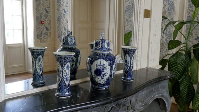 Three vases being displayed on the corner of the house. Located on the side of the house where ther is a mirror and a plant on the side