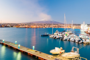 Skyline of Catania and its harbor with snowy volcano Etna in background after the sunset