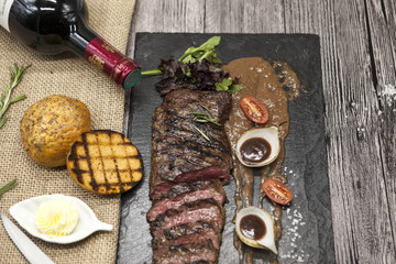 Delicious juicy hot roast beef cut into delicious pieces of meat and vegetables. Served on a black stone plate with a fork and knife and pepper and wine