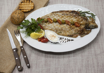 Fried fish whitefish on plate with vegetables and bread with a fork and knife.