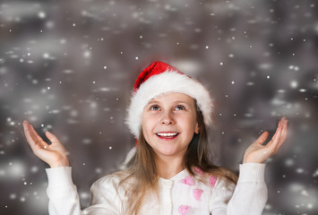 Cute little girl in a Christmas hat enjoys the falling snow