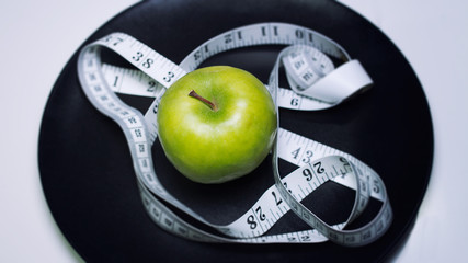 Bright green apple with white measuring tape on a black background, diet concept, healthy lifestyle