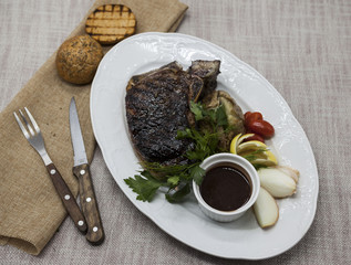 Ribeye steak from marble beef meat with vegetables and barbecue sauce. Served on a plate of black stone with fork and knife .