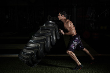 Fototapeta na wymiar Crossfit training. Young sportsman with muscular body lifting heavy wheel in gym.
