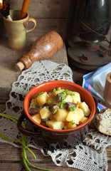 Country still life with an old kerosene lamp, pan with potatoes and chicken hearts, bread and spring onions. Selective focus and toned.