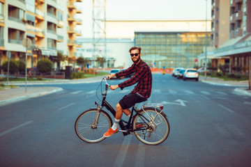 Stylish man in sunglasses riding a bike on city street