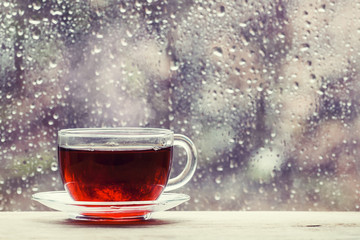 Cup of hot black tea on the blurred background of wet window on