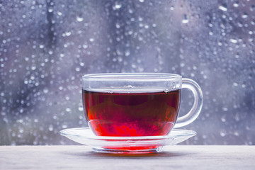 Cup of hot black tea on the blurred background of wet window on