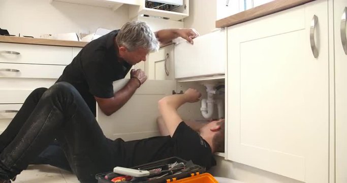Plumber teaching apprentice to fix kitchen sink