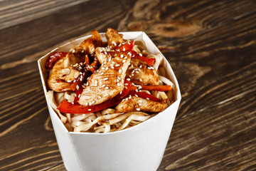 Delicious wok noodles box container with udon and chicken on wooden table. Chinese and asian takeaway fast food. 