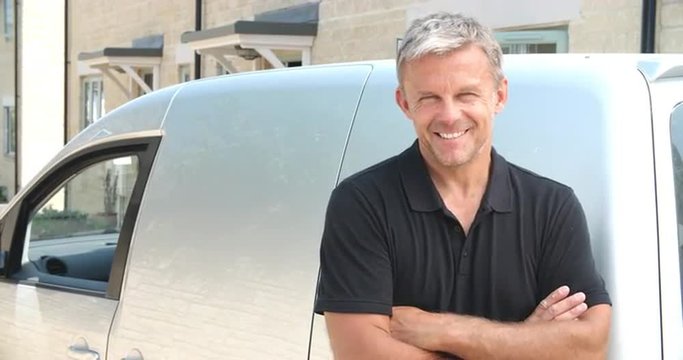 Middle aged tradesman in front of his van, panning up shot