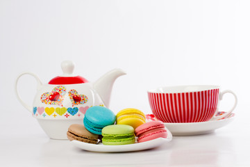 Collection of brightly colored French macarons on white background, lying in a saucer, standing next to the kettle