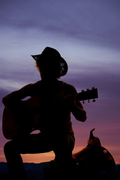 silhouette of a cowboy sitting on a saddle playing a guitar