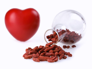 Goji berries inside and outside a glass jar, and a heart in the background