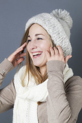 trendy warm winter - giggling young blond girl getting warmer with white wool winter scarf and hat enjoying softness and comfy fashion