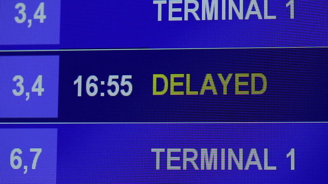Airport departure board in terminal with "DELAYED" flight information with English and Chinese language