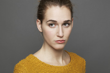 negative feelings concept - portrait of unhappy beautiful 20s girl expressing doubt and sadness,studio shot on gray background