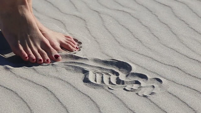 Beautiful female legs playing with sand on the sandy sea beach