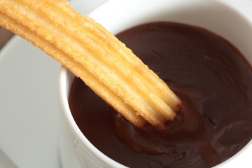 cup of liquid chocolate and churros on a wooden table