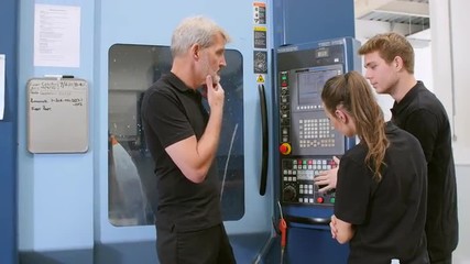 Two Apprentices Working With Engineer On CNC Machinery