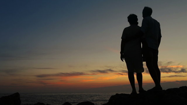Couple standing on the cliff of a mountain holding hands and watching sunset