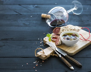 Wine appetizer set. Glass of red wine, French sausage and olives on black wooden backdrop