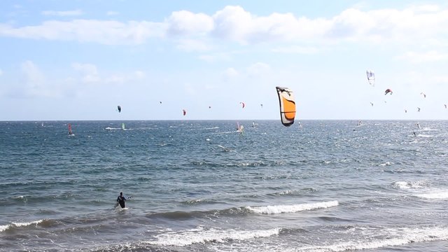 Kitesurfer at beach holding his kite in wind , many surfer in background