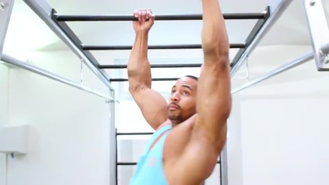 Muscular young man exercising on monkey bars at a gym
