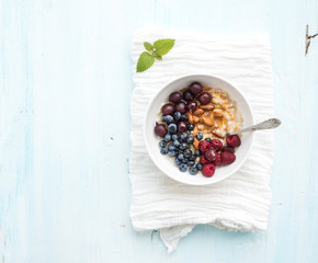 Healthy breakfast set. Bowl of oat porridge with fresh berries, almond and honey over white napkin. Top view, light blue backdrop